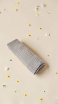 Cloudy Cotton grey muslin swaddle blanket made from soft breathable cotton, rolled on a beige background with flowers.