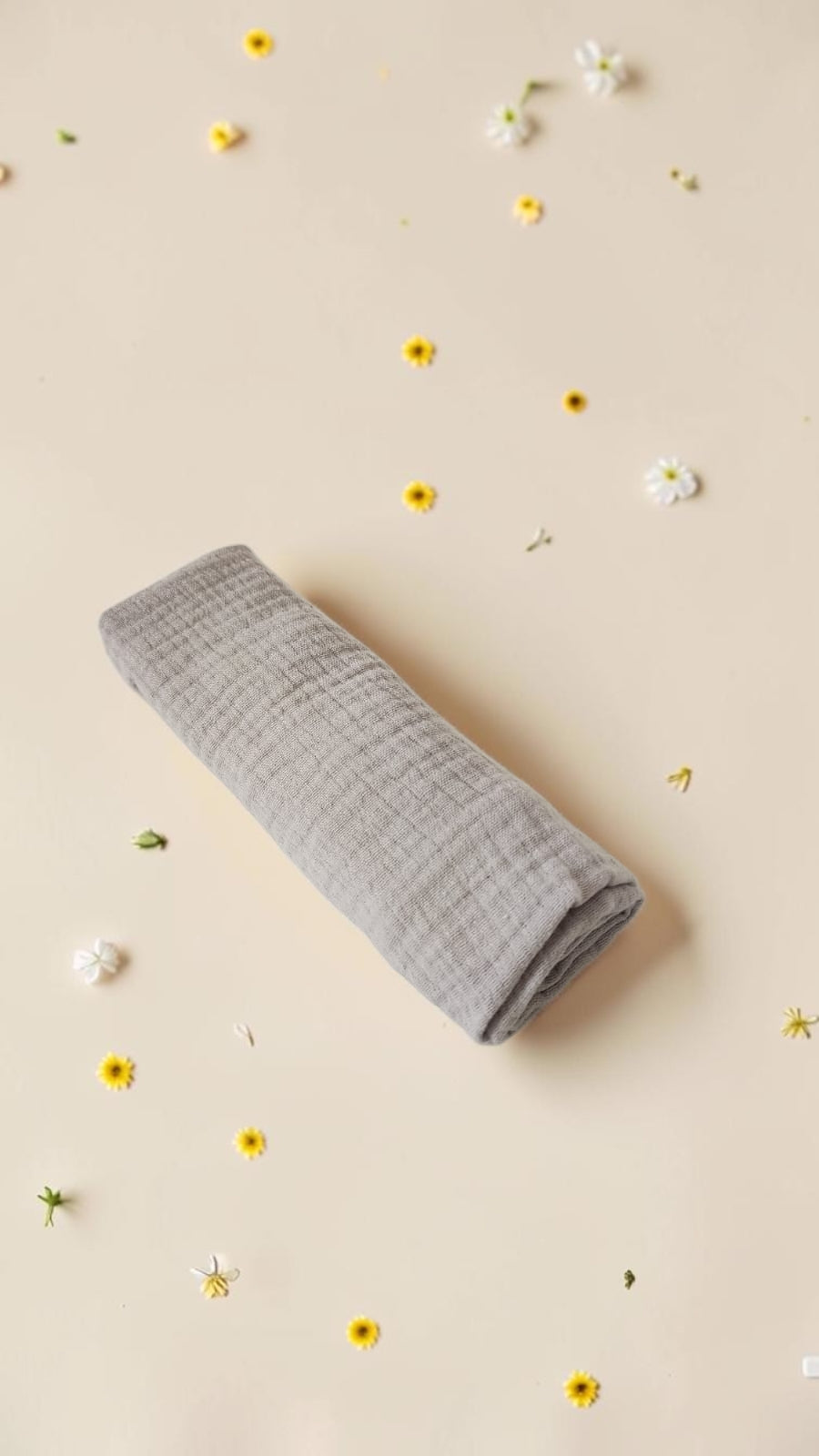 Cloudy Cotton grey muslin swaddle blanket made from soft breathable cotton, rolled on a beige background with flowers.