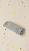 Cloudy Cotton sage green organic muslin swaddle blanket with a soft, breathable texture on a floral background.