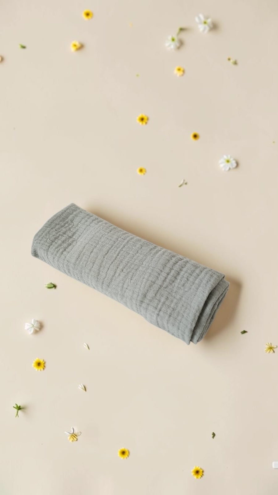 Cloudy Cotton sage green organic muslin swaddle blanket with a soft, breathable texture on a floral background.